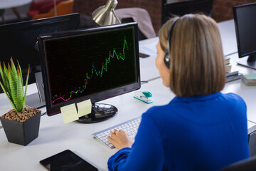 Caucasian businesswoman sitting at desk using computer with statistical data on screen