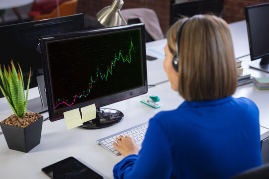 Caucasian businesswoman sitting at desk using computer with statistical data on screen