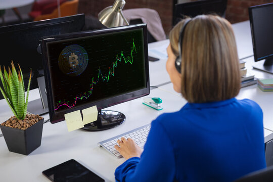 Caucasian businesswoman sitting at desk using computer with statistical data on screen