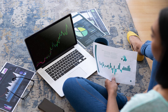 Biracial woman sitting on floor using laptop with statistical data on screen