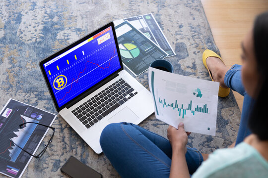 Biracial woman sitting on floor using laptop with statistical data on screen
