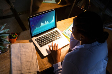 Biracial businesswoman sitting at desk using laptop with statistical data on screen