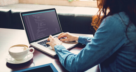 Midsection of caucasian female programmer sitting at desk and using laptop with coding on screen