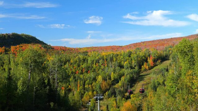 Autumn leaf colors on a hill in northern Minnesota as red gondola for tourists and skiers go up and down the mountain, on a sunny fall day near the north shore of Lake Superior.