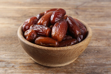 Sweet dried dates in bowl on wooden table, closeup