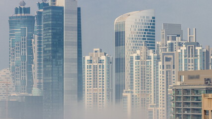 Dubai skyscrapers covered by morning fog in business bay district during sunrise timelapse.