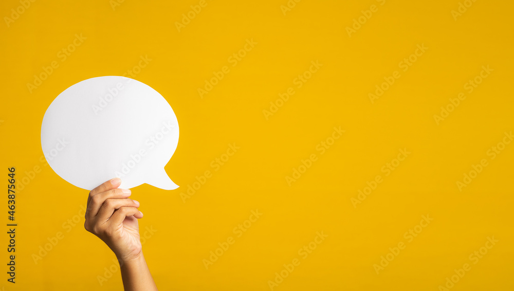 Poster concept of a speech bubble. hand holding an empty speech bubble on yellow background with copy space