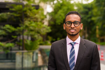 Portrait of handsome young African businessman smiling outdoors in city