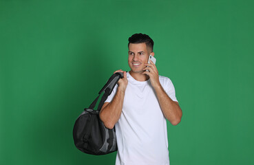 Handsome man with sports bag and smartphone on green background