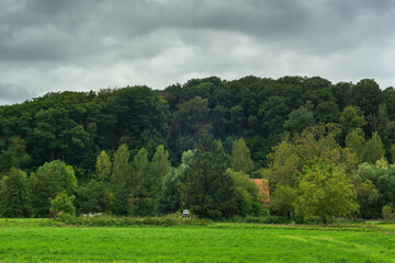 House with an off road vehicle on the edge of a hilly forest under a dark cloudy sky.