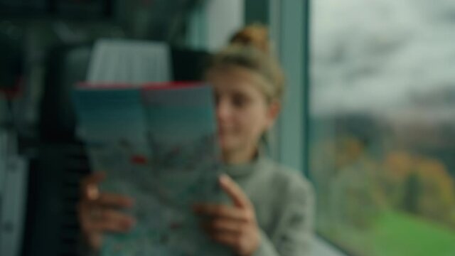 Woman travel solo look out of window of scenic train. Look at landmarks tourist map. Cinematic and inspiring travel blogger live motivational adventure. Happy young woman on train vacation. Soft focus
