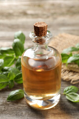 Glass bottle of basil essential oil and leaves on wooden table, closeup