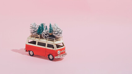 A Christmas arrangement made of red van, Christmas trees and cones on a pastel pink background....