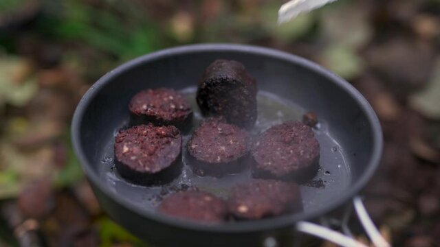 Black pudding frying in a pan while camping in the woods