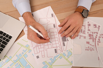 Professional cartographer working with cadastral map at wooden table, top view