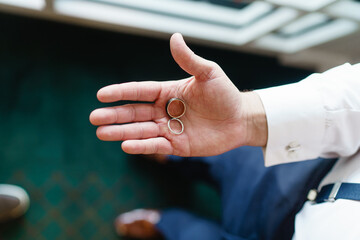 Wedding rings lie in the groom's palm close-up Top view Two gold wedding rings lying on the open palm of a young groom in blue trousers Wedding tradition and symbol Pair Of Golden Rins cropped view
