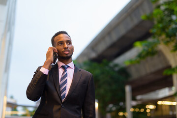 Young African businessman outdoors in city talking on mobile phone