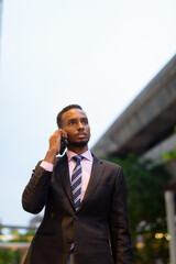 Young African businessman outdoors in city talking on mobile phone