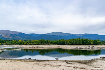 Fototapeta na wymiar Reservoir. Views of a reservoir that reflects the landscape in the water on a cloudy day in Segovia, in Castilla y León, in Spain. Europe. Horizontal photography. 