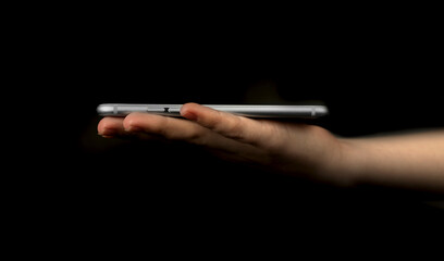 Female hand with mobile phone on a black background. Concept of presentation, mockup and template for modern technology, web network etc