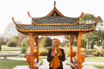 Black muslim woman meditating qigong near chinese arbor. African woman does chinese sport training outdoor.