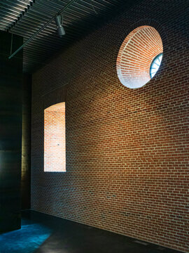 Interior de un edificio de ladrillos con ventanas cuadrada y redonda donde pasa la luz