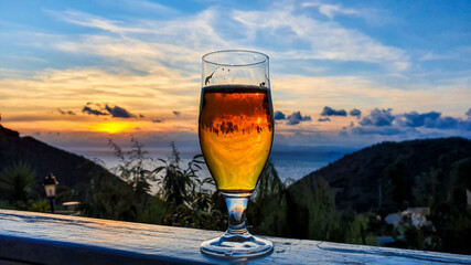 Beer glass on a wooden plate in front of a sunset by the sea