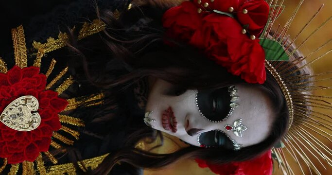 Vertical portrait of young woman with sugar skull makeup and red roses dressed in black costume of death as Santa Muerte. Day of the Dead or Halloween concept.