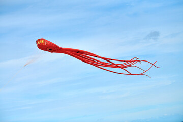 Bright red pink octopus kite flying in blue sky with clouds, red octopus-shaped kite, kite festival