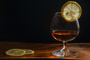 Glass of cognac close-up on a dark wooden background with lemon