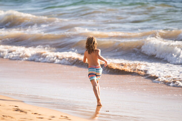 Fototapeta na wymiar Back view of kid boy jumping and running on sea beach.