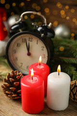 Alarm clock, burning candles and Christmas decor on wooden table, bokeh effect