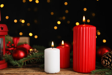 Burning candles and Christmas decor on wooden table against blurred festive lights