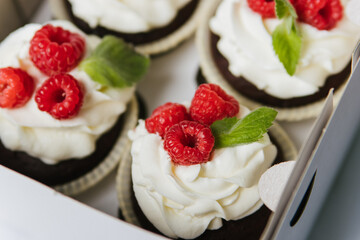 Cupcakes with white butter cream and berries lie in a box.