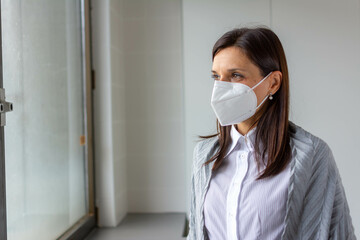 Woman in respiratory mask. Masked woman looks at window. Cold, flu, virus, tonsillitis, respiratory disease, quarantine, epidemic concept. Beautiful caucasian woman with disposable face mask.