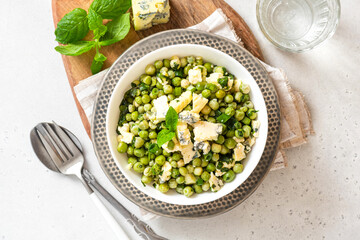 Cooked green peas with mint, onions and blue cheese in bowl on a grey background top view. Steamed green peas. French cuisine, healthy food.