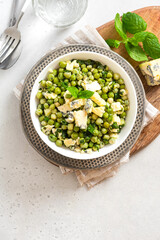 Cooked green peas with mint, onions and blue cheese in bowl on a grey background top view. Steamed green peas. French cuisine, healthy food.