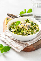 Cooked green peas with mint, onions and blue cheese in bowl on a grey background. Steamed green peas. French cuisine, healthy food.