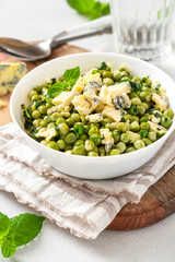Cooked green peas with mint, onions and blue cheese in bowl on a grey background. Steamed green peas. French cuisine, healthy food.