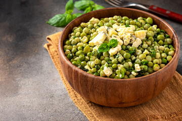 Cooked green peas with mint, onions and blue cheese in wooden bolw on a dark background. Steamed green peas. French cuisine, healthy food.