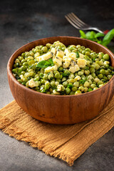 Cooked green peas with mint, onions and blue cheese in wooden bolw on a dark background. Steamed green peas. French cuisine, healthy food.