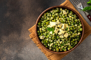 Cooked green peas with mint, onions and blue cheese in wooden bolw on a dark background top view. Steamed green peas. French cuisine, healthy food. Copy space