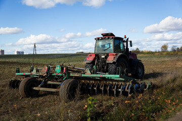 A farmer in a tractor, agricultural machinery, prepares the land with a cultivator. A modern red tractor in a field. Plowing a heavy tractor while cultivating agricultural work in a field with a plow.