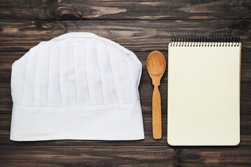 Chef hat with spoon and notepad on wooden background