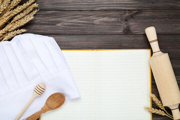 Chef hat with cooking cutlery, notepad and wheat ears on wooden background
