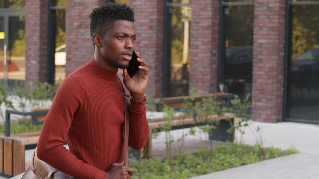 Medium slowmo shot of young African-American businessman having phone conversation outdoors trying to catch taxi in downtown area