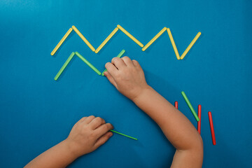 A small child creates a geometric pattern using counting sticks. Isolated on a blue background.