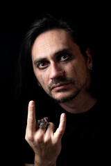 Portrait of a man with dripping eye shadow, doing metal gesture on black background. Soft focus