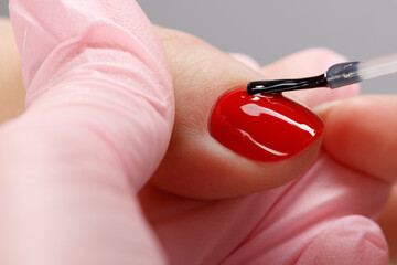 Close up process of applying transparent lacquer on a red varnish. Woman in salon receiving...