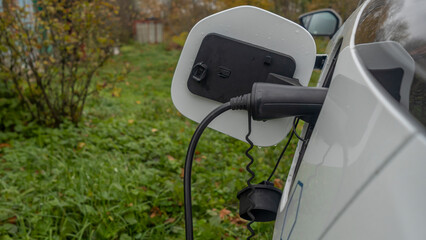 White electric car is charged in the village. Private electric car charger. Electric charge in a village house.